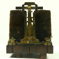 Brass apparatus with battery in centre on wooden base.