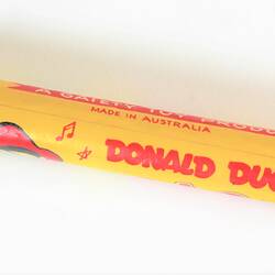 Yellow plastic toy flute with red lettering.