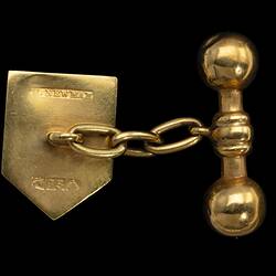 Back of gold cufflink. Heraldic shield design with centrally placed opal. Chain links to barbell.