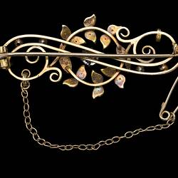 Back of central gold circle overlaying gold scroll. Fine chain and pin at left.