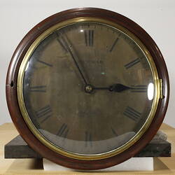 Round clock face with black numerals and wooden trim.
