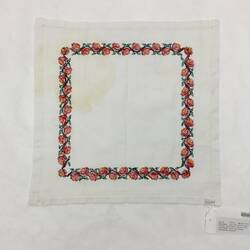 Back of off-white square cloth embroidered with an inset square margin of red roses with green leaves.