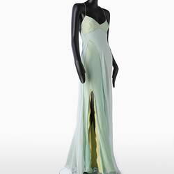 Full length pale green silk evening slip dress. Sleeveless. Fastens at back with long green silk covered rope ties. Flared/fishtail skirt with long slit at right.
