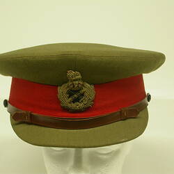 Green cap with red hat band with attached broach and leather strap on top of visor.