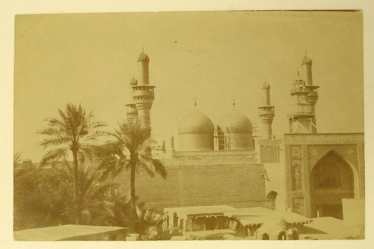Exterior of Tomb of the Imams, palm trees and low buildings surrounding it.