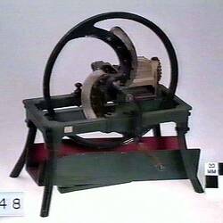 Chaffcutter model made from metal featuring large rotating wheel with two blades controlled by rotating handle.