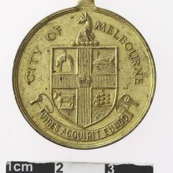 Round gold coloured medal with coat of arms, text surrounding.