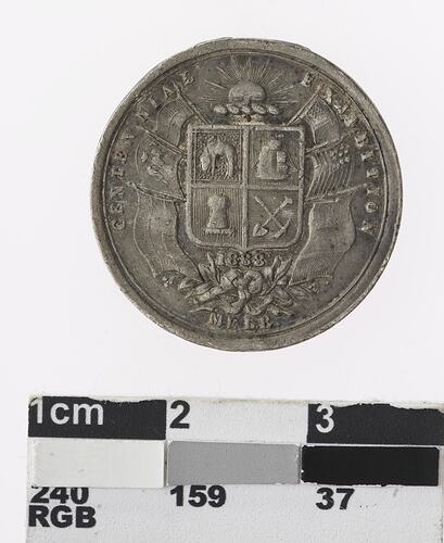 Round silver coloured medal with Australian coat of arms and flags attached to either side.