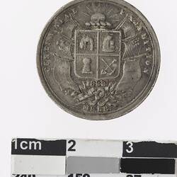 Round silver coloured medal with Australian coat of arms and flags attached to either side.