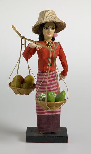 Doll in traditional costume carrying two baskets of fruit.