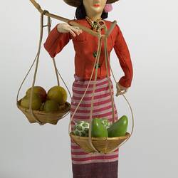 Doll in traditional costume carrying two baskets of fruit.