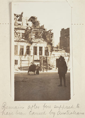 Bomb damaged building with man in foreground and man and donkey in mid ground.