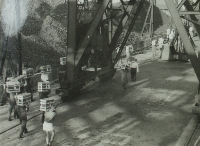 Sailors carrying wooden crates with large steel framed structure on road.
