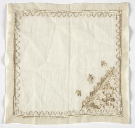 Square, white cloth with gold embroidery.