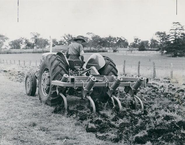 Rear view of a man driving a tractor coupled to a tiller.