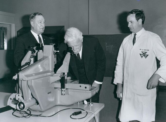 Three men standing next to metallurgical microscope.