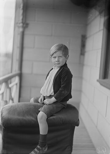 Boy sitting astride a soft box on a house veranda.