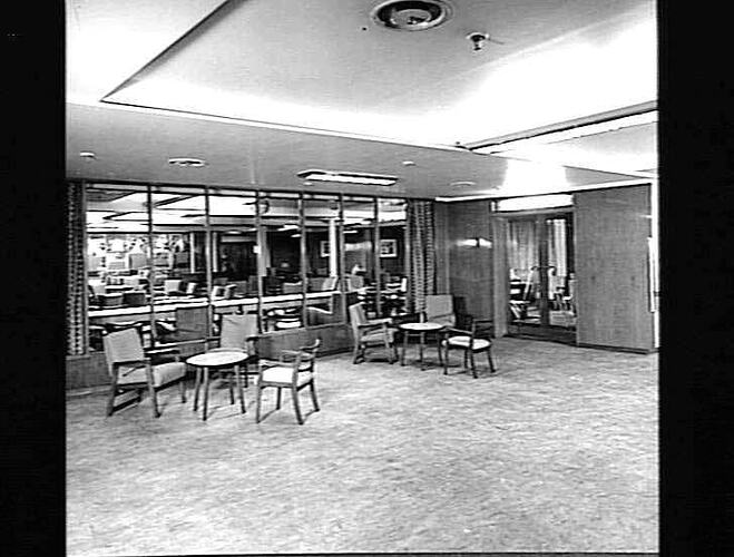 Ship interior. Room with upholstered chairs around tables. Windows in background. Lounge area.