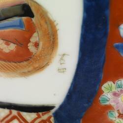 Detail of white vase with two brown Chinese characters surrounded by red, blue, green, orange and pink decoration.
