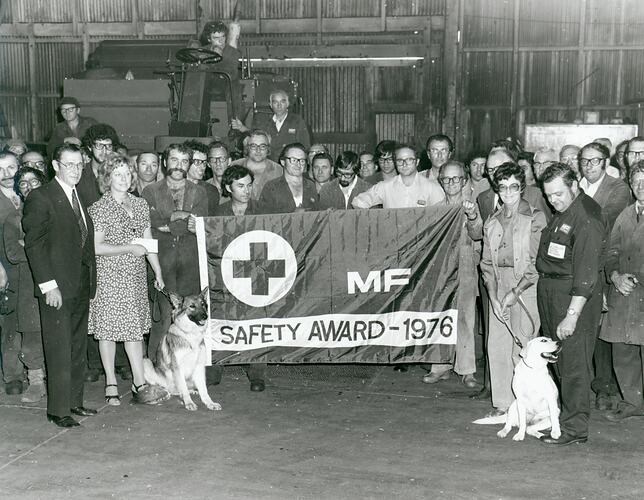 A large group of people stand behind a flag displaying MF Safety award.
