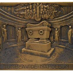Rectangular bronze plaque. Raised coffin in centre of round room with columns and statues. Engraved text below