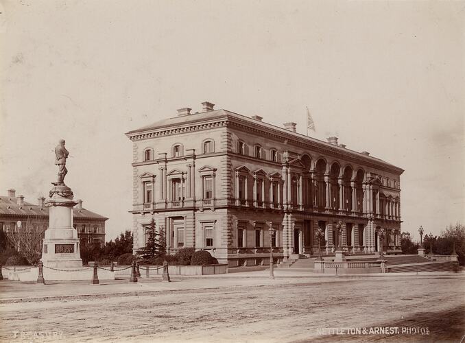 Corner view of 3 storey building with British flag. Front entrance and surrounding garden. Statue at left.