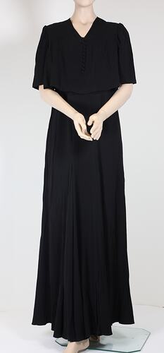 Front view, long black dress with elbow sleeves.