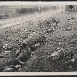 Ditch on side of road with items strewn on ground and bodies of deceased soldiers.