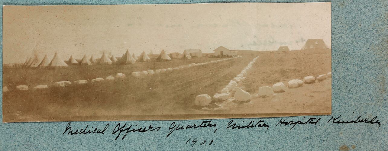 Road marked by white rocks with large group of tents on left.