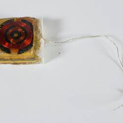 Bionic ear prototype. Yellow square with red circular centre. Clear wire coming out at right side.
