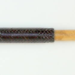 Wooden stick covered halfway along length with black braiding. Brown braided knob on end.