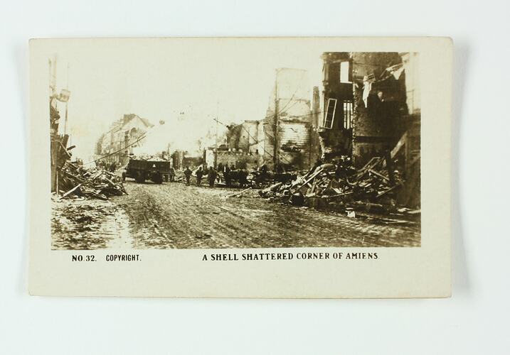 Soldiers and a truck on a street with debris from houses either side.