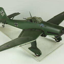 Model aeroplane. Dark green with black cross on side, wing tips and tail. Black propeller.