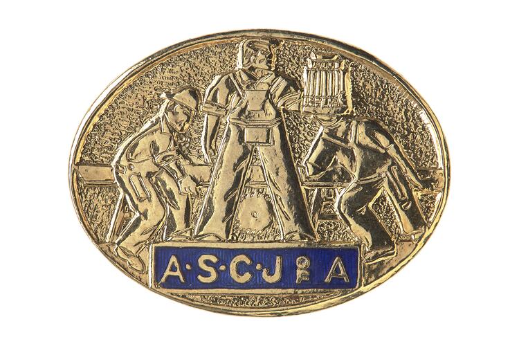 Brass oval badge with relief of 3 men working with timber and a saw. Blue enamel banner at base has gold text.