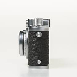 Black camera with metal trim, lens, dials at top corners. Left profile.