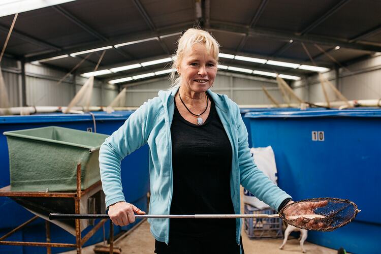 Woman in shed holding a fish in net.