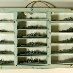 One half of a wooden bifold case painted blue-grey with rope handle. Contains 16 grey ship models in 3 columns