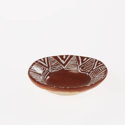 Miniature brown ceramic plate. Features white painted patterns around rim.