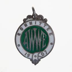 Round metal medal with white enamel border, green centre. Text around and in centre.