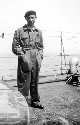 Man wearing a beret and boiler suits stand on a ship's deck. Ocean in the background.