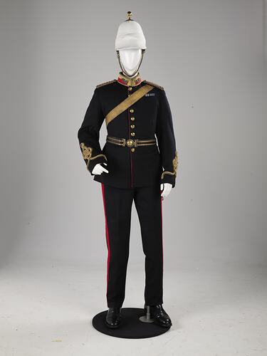 Navy officer's uniform with gold at cuff, epaulettes, belt. Brass buttons. Red/gold collar. White helmet.