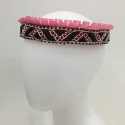 Round beaded crown on mannequin head. Pink ruffled ribbon trim around the top. Green and white plastic beads.