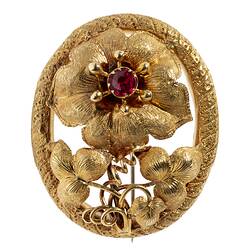 Gold brooch with large flower with red centre, supported by two lower leaves and tendrils, inside an oval border.
