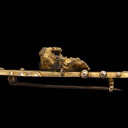 Profile of gold double bar brooch with decorative detailing. Features small natural nugget in centre.