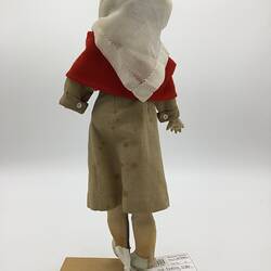A doll dressed as a nurse in a brown dress, red capelet and white scarf
