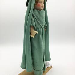 A doll dressed in a long green gown, veil and hat