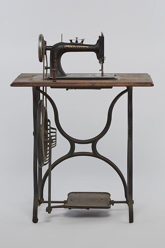Sewing machine fitted to a metal frame with a wooden bench.