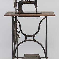 Sewing machine fitted to a metal frame with a wooden bench.