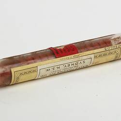 Glass tube, metal lid. Contains red tablets. Paper labels with text affixed to tube.