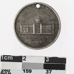 Round silver coloured medal with building and text, details faded.